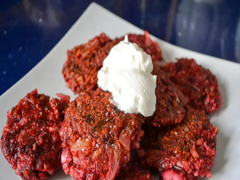 Pequenos latkes de beterraba, dourados por fora, com iogurte e folhas verdes.